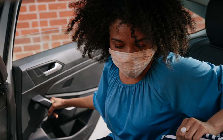 Woman wearing Covid mask entering the back seat of a Lyft ride after a health care appointment