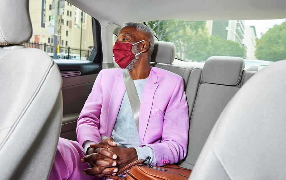 Stylish man happily looking out the car window wearing a covid mask while using Lyft to commute