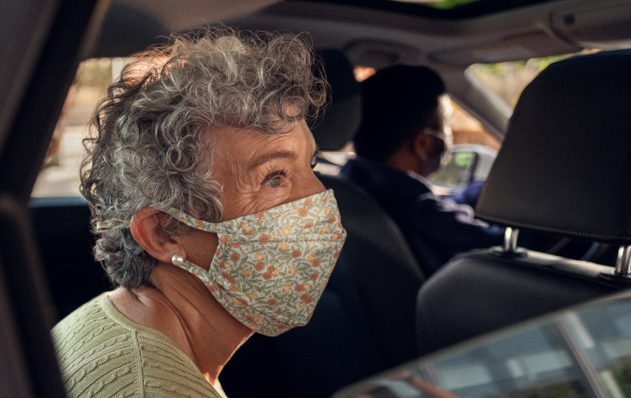 Older woman happily looking out of a car window, wearing a covid mask during her Lyft ride