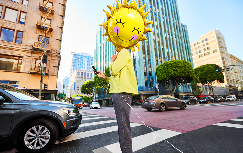Person holding a bright smiling sun balloon while waiting for their Lyft Ride on a city street